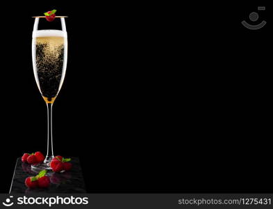 Elegant glass of yellow champagne with rasspbery and fresh berries with mint leaf on stick on black marble board on black.