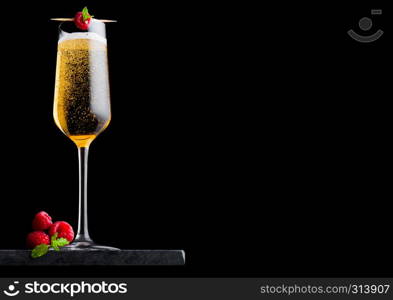 Elegant glass of yellow champagne with rasspbery and fresh berries with mint leaf on stick on black marble board on black.