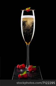Elegant glass of yellow champagne with rasspbery and fresh berries with mint leaf on stick on black marble board