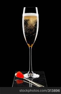 Elegant glass of yellow champagne with red caviar on golden spoon of caviar on marble board on black.