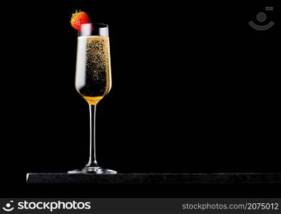 Elegant glass of yellow champagne with strawberry on top on black marble board on black background.