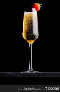 Elegant glass of yellow champagne with strawberry on top on black marble board on black.