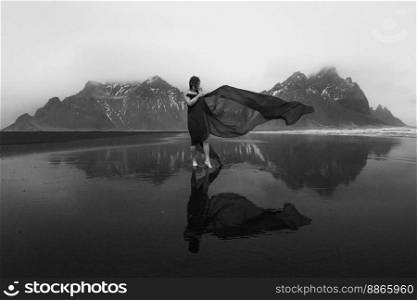 Elegant lady with long waving cape on beach monochrome scenic photography. Picture of person with hills on background. High quality wallpaper. Photo concept for ads, travel blog, magazine, article. Elegant lady with long waving cape on beach monochrome scenic photography