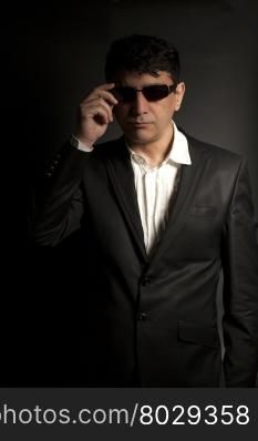 Elegant man with sunglasses wearing black suit on black background