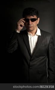 Elegant man with sunglasses wearing black suit on black background