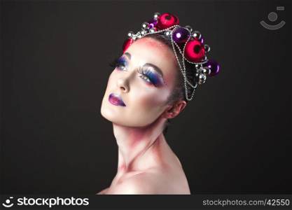 Elegant model with bright New Year's Eve make-up in a wreath of Christmas toys. Studio shot.