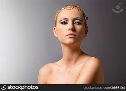 elegant msake-up blonde woman in beauty portrait with naked shoulders wearing metal jewellery on the head. Looks in camera