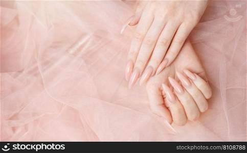 Elegant pastel pink natural manicure. Female hands  on pink silk background.