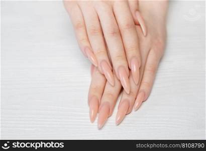Elegant pastel pink natural manicure. Female hands  on white wooden background.