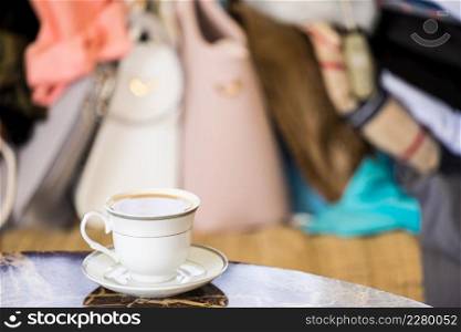 Elegant retro styled coffee cup on wooden table, colorful purse bags in background.. Elegant coffee cup on table
