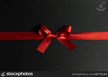 Elegant satin red ribbon bow on black background. Red ribbon bow on black