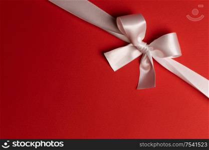 Elegant satin white ribbon bow on red background. White ribbon bow on red