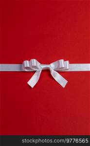 Elegant satin white ribbon bow on red background wih copy space. White ribbon bow on red
