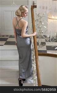 elegant sensual blond girl in evening dress , going up stair , and looking down , with aristocratic look