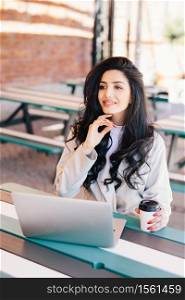 Elegant successful woman freelancer dressed formally using generic laptop computer for remote work, having rest at outdoor cafe drinking delicious coffee having dreamy expression. Lifestyle concept