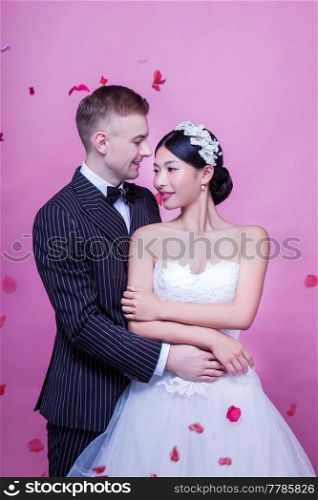 Elegant wedding couple embracing while standing against pink background