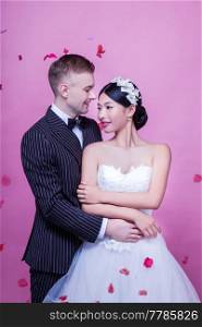 Elegant wedding couple embracing while standing against pink background