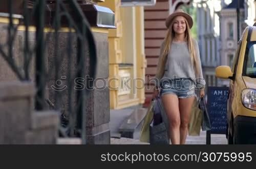 Elegant woman carrying shopping bags and smiling while walking along the street