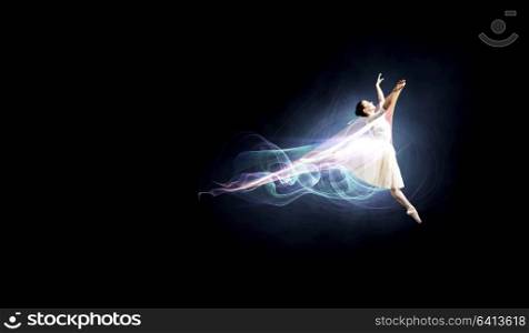 Elegant woman dancer in white dress against dark background. Ballet dancer in jump