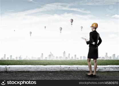 Elegant woman engineer. Young woman architect in hardhat holding project in hand