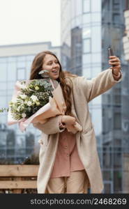 elegant woman holding bouquet flowers outside taking selfie with smartphone