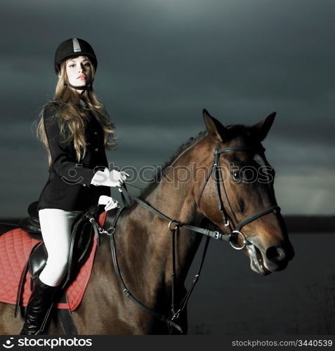 Elegant woman in a black coat riding on a brown horse