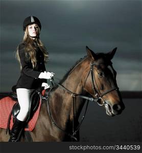 Elegant woman in a black coat riding on a brown horse