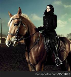 Elegant woman in a black coat riding on a brown horse