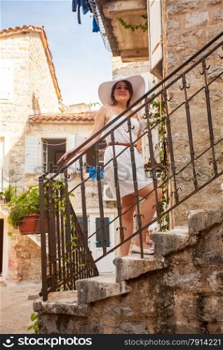 Elegant woman in hat posing on beautiful stairs at narrow street