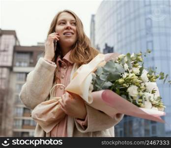 elegant woman outdoors talking smartphone holding bouquet flowers