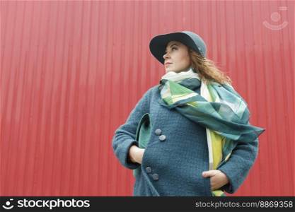 Elegant woman wearing hat and coat posing on city street near wall