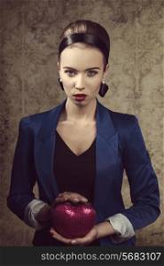 elegant woman with blue jacket and creative hair-style posing in front of camera with small romantic heart shaped bag in the hand