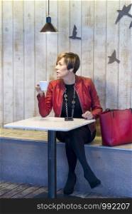 Elegant woman with red jacket sitting in a cafe drinking coffee.