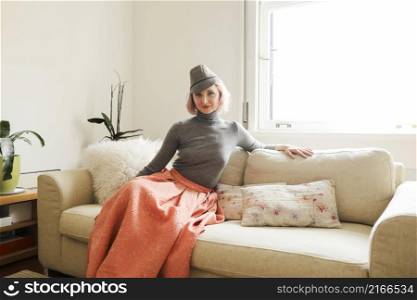 Elegant woman woman wearing pink skirt and hat while sitting on sofa