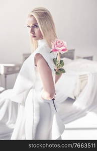 Elegant, young blond lady holding a beautiful pink rose