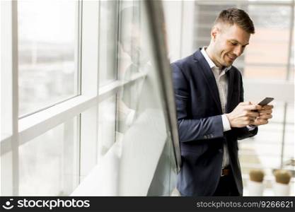 Elegant young businessman using cellphone on staircase in office