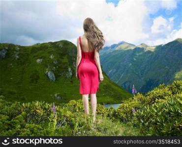 Elegant young lady in a red dress on a mountain meadow flower