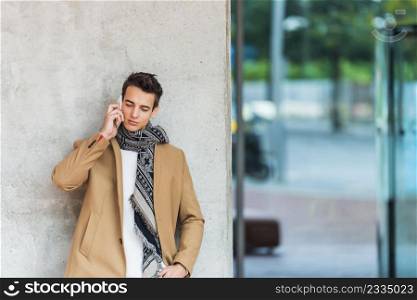 Elegant young man leaning on wall while using mobile phone