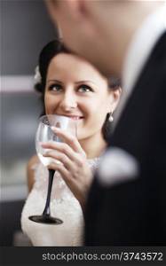 Elegant young woman in a white dress drinking white wine at a function and smiling up at her male partner