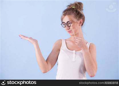 Elegant young woman pretending wearing funny nerd eyeglasses showing copy space on hand. Education and studying females look concept.. Elegant woman pretending wearing eyeglasses