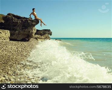 Elegant young woman sits on rocky shore