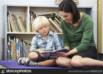 Elementary Pupil Reading With Teacher In Classroom