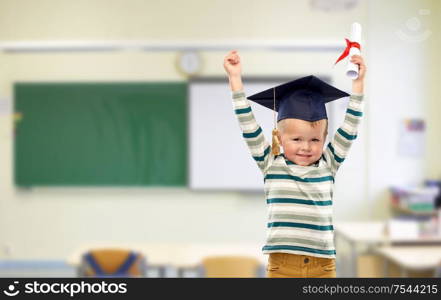 elementary school, preschool education and success concept - portrait of smiling little boy in mortar board with diploma celebrating triumph over classroom background. little boy in mortar board with diploma at school