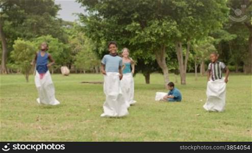 Elementary school teacher and kids having fun and playing sack race in city park