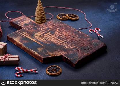 Elements of Christmas decorations, sweets and gingerbread on a wooden cutting board against a dark concrete background. Preparing for the holiday. Elements of Christmas decorations, sweets and gingerbread on a wooden cutting board