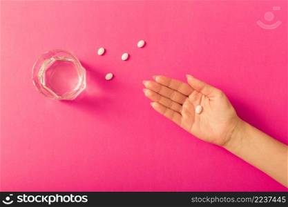elevated view female s hand taking medicine with water glass pink background