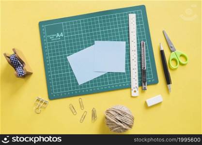 elevated view green cutting mat stationeries yellow background