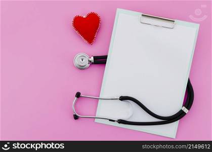 elevated view hand made red heart with stethoscope clipboard pink background