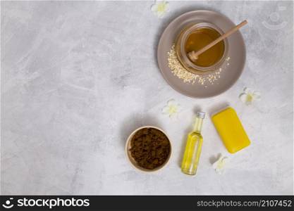 elevated view honey yellow soap essential oil bottle coffee powder with white flowers concrete backdrop