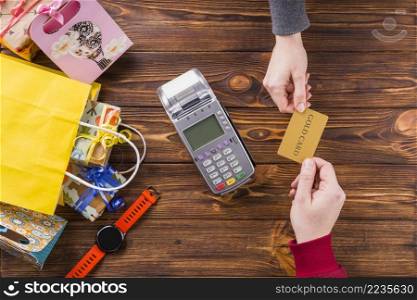 elevated view human hands holding gold card with swiping machine wooden table